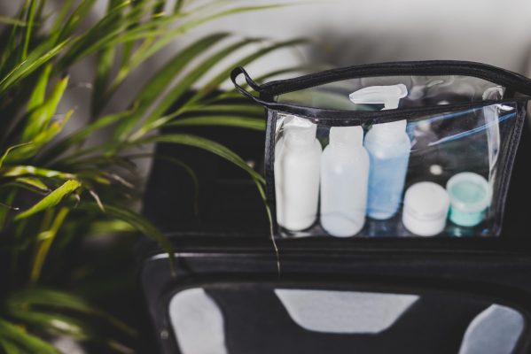 packing for a flight and airport screening concept, transparent bag with small lotions for liquids and gel for security check compliance on top cabin luggage and with palm tree next to it