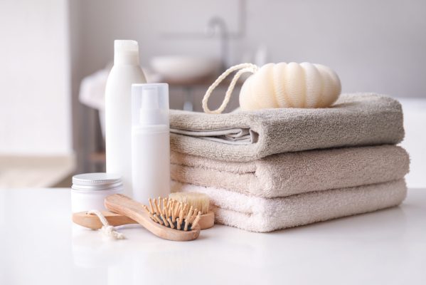 Stack of towels, cosmetics, loofah and brushes on table in bathroom