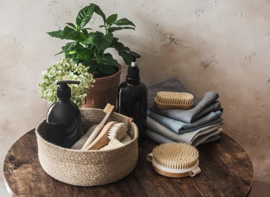 Bathroom interior still life. Natural bristle brush, shampoo bottle, towels, flower on dark background