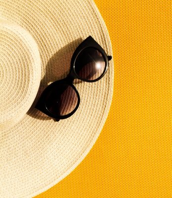 Beautiful straw hat with sunglasses on yellow vibrant vivid background. Top View. Flat Lay. Summer Travel Vacation Concept.