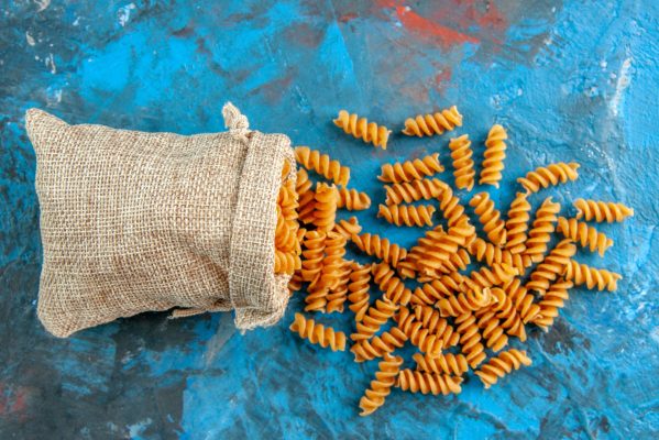 close-up-view-of-raw-italian-pastas-from-the-gray-purse-on-the-right-side-on-blue-background