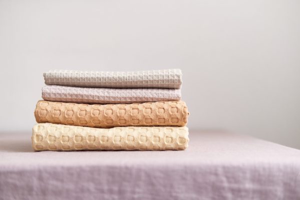 Collection of natural muslin kitchen towels stacked neatly in a vertical stack. Natural, soft, airy and stylish kitchen textiles. Front view.