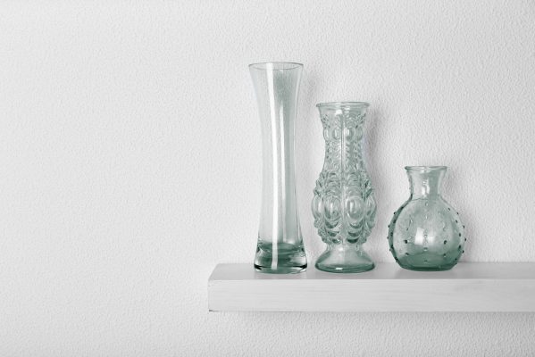 Decorative glass vases on wooden shelf  on white wallpaper background