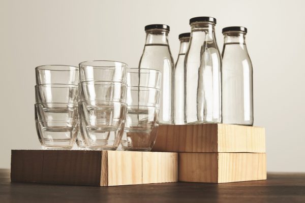 Perfect set of pure clean healthy water in transparent glass bottles and cups presented on wooden plates on table