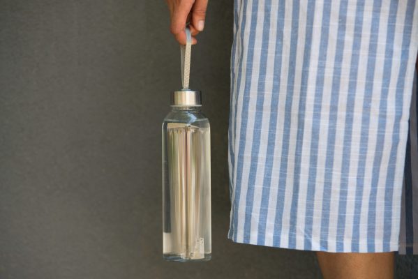 woman is holding and drinking from glass reusable bottle with clear water